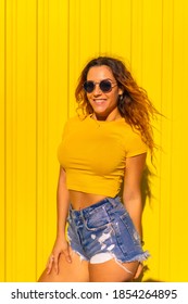 Lifestyle, Caucasian Blonde Girl In Yellow T-shirts And Short Jeans On A Yellow Background. Fashionable Posing With A Smile, Street Photography