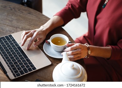 Lifestyle And Citylife - Hands Closeup Of Business Lady Working On Laptop And Holding Cup Of Tea In Cafe While Having Lunch. Woman Sits By The Table With Portable Computer