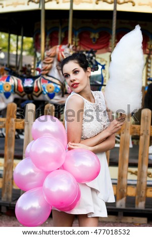 Lifestyle concept, attractive teenager with colorful latex balloons in the amusement park near carousel with cotton candy
