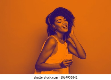 Lifestyle Concept - Portrait of beautiful African American woman joyful listening to music on mobile phone. Yellow pastel studio background. Copy Space and Duotone.