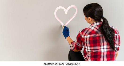 Lifestyle creative hobby and freelance artistic work concept. Caucasian woman artist painting heart shape on walls indoor at apartment or studio with acrylic paints 
