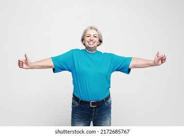 Lifestyle, emotion and people concept: Elderly happy female wearing jeans and blue shirt giving a thumb up and looking at the camera