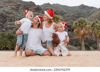 Lifestyle family portrait on ocean beach in Christmas Santa Claus Red Hats Caps. Christmas or New Year vacation and holidays. Family with kids spending time together outdoors. - Powered by Shutterstock