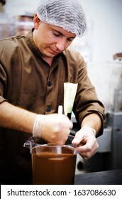 Lifestyle food photography of a caucasian male chocolatier stirring chocolate in a jug that he has just tempered in a chocolate factory