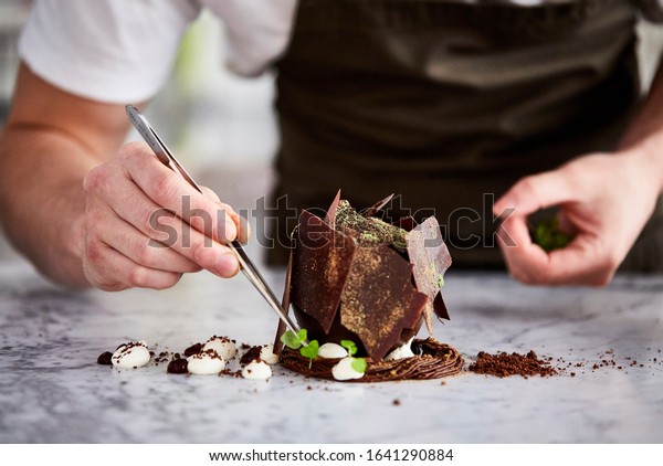 Lifestyle\
food photography of a light skinned male chef plating up a fine\
dining chocolate dessert on a marble\
surface