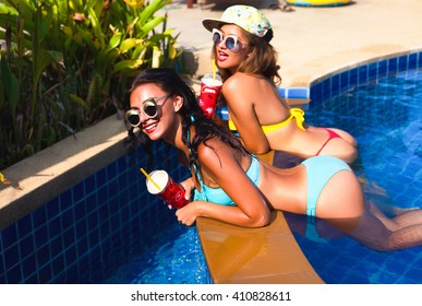 Lifestyle image of two young pretty friends girls having fun outdoor on the pool of summer on the party.Sitting on pool on fashionable swimsuits,conversation, laughing, Positive mood.Friendship