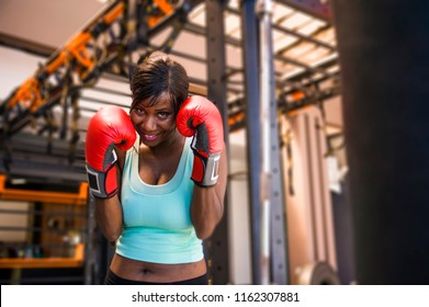 lifestyle indoors portrait of young attractive and beautiful black afro American woman training happy in gym with heavy bag punching wearing boxing gloves at modern and cool fitness club  - Powered by Shutterstock