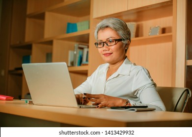 lifestyle office portrait of attractive and happy successful middle aged Asian woman working at laptop computer desk smiling confident in entrepreneur business and financial success 