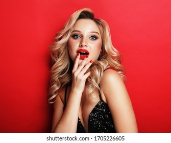 lifestyle, party and people concept - Gorgeous blonde woman in an evening dress flirty and playful on a red background - Powered by Shutterstock