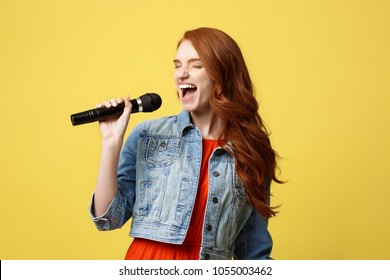 Lifestyle and People Concept: Expressive girl singing with a microphone, isolated bright yellow background.