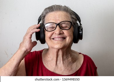 Lifestyle and people concept: Funny old lady listening music and dancing on white background. Elderly woman wearing glasses dancing to music listening on his headphones.