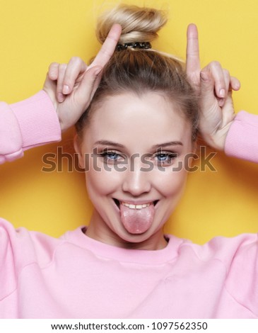 lifestyle and people concept: Look at me like I'm funny. Portrait of a young beautiful girl on a yellow background with a smiling showing horns on the camera. She smiles and looks happy. Happy time.