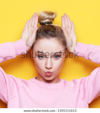 lifestyle and people concept: Look at me like I'm funny. Portrait of a young beautiful girl on a yellow background with a smiling showing horns on the camera.