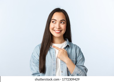 Lifestyle, People Emotions And Beauty Concept. Intrigued Cute Asian Female Customer Checking-out New Discount Promotion, Pointing Finger Left And Looking At Product Excited, Smiling