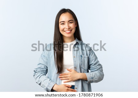 Lifestyle, people emotions and beauty concept. Pleased smiling asian woman rubbing her belly, being full after eating, pleased feeling in stomach from drinking yoghurt