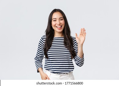 Lifestyle, people emotions and casual concept. Friendly cheerful asian woman smiling, saying hi and waving hand to greet person, make hello gesture, welcome someone