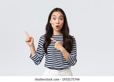 Lifestyle, people emotions and casual concept. Surprised and excited cute asian female customer telling about big sale, promo discounts, pointing fingers upper left corner and look amazed - Shutterstock ID 1933175744