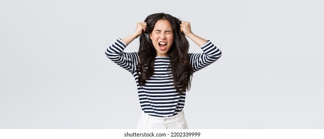 Lifestyle, People Emotions And Casual Concept. Pissed-off Mad And Angry Asian Young Woman Tossing Hair, Pulling It From Head With Screams And Closed Eyes, Standing Bothered White Background