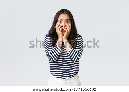 Lifestyle, people emotions and casual concept. Scared timid and insecure woman hold hands near mouth, screaming and looking terrified, shivering from fear, stand white background