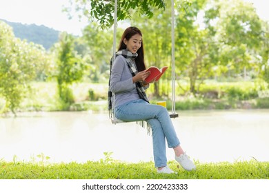 Lifestyle People Girl Reading Book And Drinking Coffee For Education Outdoor Garden At Home. Young Asian Woman Sitting Swing Chill And Resting In Summer Vacations.