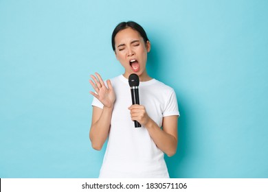 Lifestyle, People And Leisure Concept. Carefree Beautiful Asian Girl Singing Sing In Microphone With Passionate Expression, Close Eyes And Gesturing While Performing, Like Karaoke