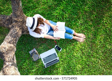 Lifestyle person Girl enjoy listening music and reading a book and play laptop on the grass field of the nature park in the morning (greenery tone). Concept lifestyle