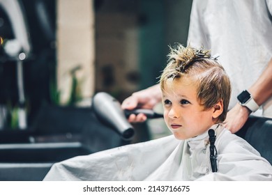 Lifestyle Photo Barber Shop Blond Boy Customer. Hairdresser Man Work Move Hand Comb Tool Scissors Dryer Clip White Cape. Modern Style Kid Short Hair Cut. Fashion Business Service For Children