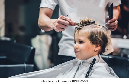 Lifestyle photo Barber shop blond boy customer. Hairdresser man work move hand comb tool scissors dryer clip white cape. Modern style kid short hair cut. Fashion business service for children - Powered by Shutterstock