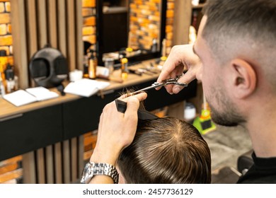 Lifestyle photo Barber shop blond boy customer. Hairdresser man work move hand comb tool scissors dryer clip white cape. Modern style kid short hair cut. Fashion business service for children - Powered by Shutterstock