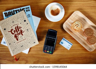 Lifestyle Photograph Of EFT Credit Card/debit Card Machine Sitting On A Shop Counter Overhead With Credit Card, Books, Espresso Coffee And Tray Of Pastries