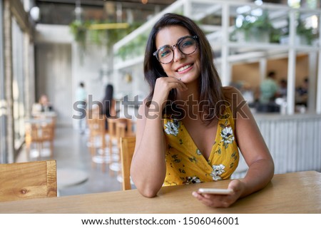 Lifestyle portait of confident beautiful natural brunette hispanic millennial vlogger sitting in modern restaurant smiling at camera