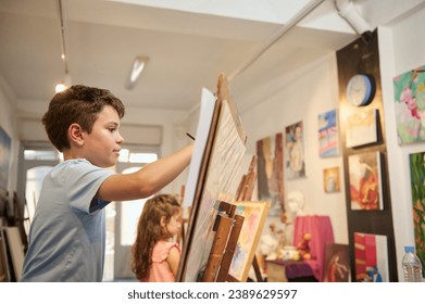 Lifestyle portrait of adorable talented kids learning drawing on canvas in a modern creative fine art studio. Children at art class in workshop with pictures exhibited on a wall in art gallery - Powered by Shutterstock