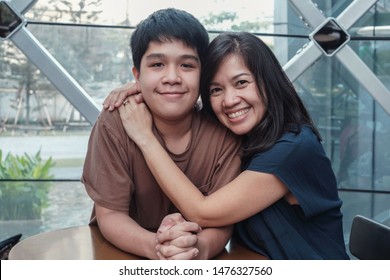 Lifestyle Portrait Of Asian 40s Mother And Son, Teenage Boy Hugging And Spending Time Together In An Urban Cafe