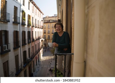 Lifestyle Portrait Of Cheerful Mature And Healthy Woman 60 To 65 Years Old Relaxed On Home Balcony Drinking Coffee Or Tea Looking To The Street In Healthy Retirement Concept