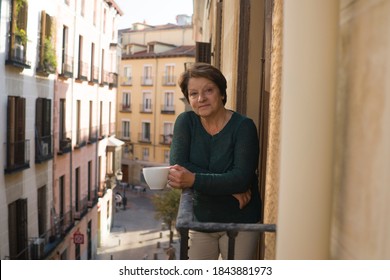 Lifestyle Portrait Of Cheerful Mature And Healthy Woman 60 To 65 Years Old Relaxed On Home Balcony Drinking Coffee Or Tea Looking To The Street In Healthy Retirement Concept