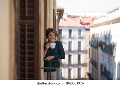 Lifestyle Portrait Of Cheerful Mature And Healthy Woman 60 To 65 Years Old Relaxed On Home Balcony Drinking Coffee Or Tea Looking To The Street In Healthy Retirement Concept