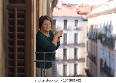 Lifestyle Portrait Of Cheerful Mature And Healthy Woman 60 To 65 Years Old Relaxed On Home Balcony Drinking Coffee Or Tea Looking To The Street In Healthy Retirement Concept