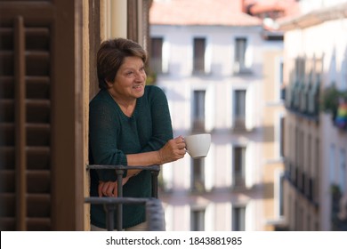 Lifestyle Portrait Of Cheerful Mature And Healthy Woman 60 To 65 Years Old Relaxed On Home Balcony Drinking Coffee Or Tea Looking To The Street In Healthy Retirement Concept