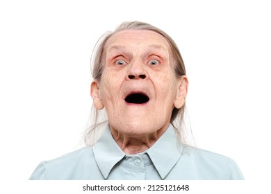 Lifestyle Portrait Of An Elderly Woman With An Open Mouth On A White Background. Grandma Looks At The Camera And Is Surprised. Old Pensioner With A Scared Expression Face. Concept Of Emotional Shock.