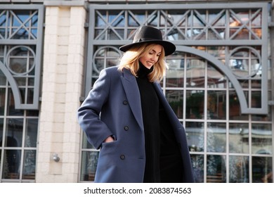 Lifestyle portrait of fashionable woman wearing winter or spring outfit, felt hat, gray wool coat, turtleneck. Outdoors. Female stylish Model smiling, walking city Street. Fashion trend