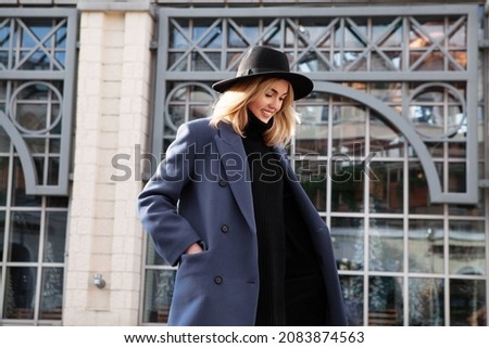 Lifestyle portrait of fashionable woman wearing winter or spring outfit, felt hat, gray wool coat, turtleneck. Outdoors. Female stylish Model smiling, walking city Street. Fashion trend