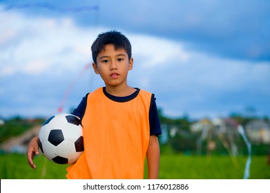 lifestyle portrait of handsome and happy young boy holding soccer ball playing football outdoors at green grass field smiling cheerful wearing training vest in kid education sport concept - Powered by Shutterstock