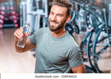 Lifestyle portrait of handsome muscular man drinking water in the gym
