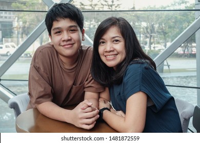 Lifestyle Portrait Of Happpy Asian 40s Mother Parent And Teenage Boy Son Spending Time Together In An Urban Cafe