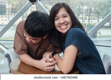 Lifestyle Portrait Of Happy Asian 40s Mother Parent And Teenage Boy Son Spending Time Together In An Urban Cafe