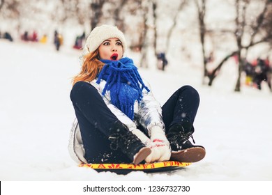 Lifestyle Portrait Of Pretty Young Woman Sliding Down Hill On Snow Saucer Sled Outdoors In Winter. Funny Face. Emotional Photo. Winter Sports With Snow. Sledding - Fun In The Mountains. Winter Fun 