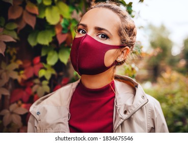 Lifestyle Portrait Of Pretty Young Woman Wearing Stylish Facial Mask And Dress The Same Vinous Color. Facial Mask For Virus Protection In Time Of Carantine. Girl Walking Outdoors In The Autumn Park
