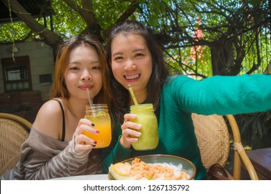 Lifestyle Portrait Of Two Young Happy And Cute Asian Chinese Girlfriends Taking Selfie Portrait Picture With Mobile Phone Camera For Using On Internet Social Media While Having Healthy Brunch At Cafe