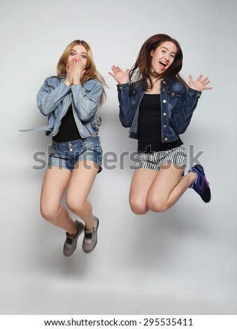 lifestyle portrait of two young hipster girls best friends jump over gray background