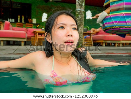 lifestyle portrait of young attractive and beautiful Asian Korean woman relaxing happy at tropical beach resort swimming at hotel pool enjoying Summer holidays in paradise island